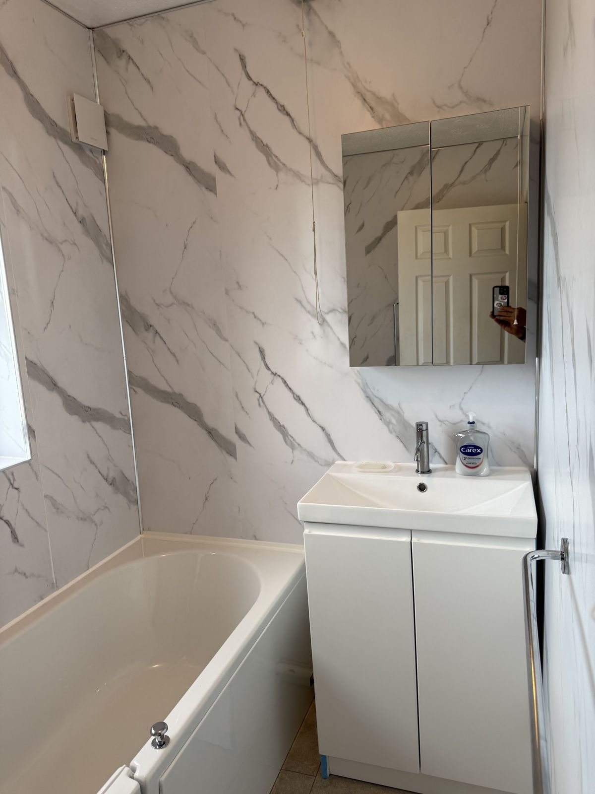 Finished bathroom with a white bath, a vanity unit, marble-effect wall panels and a mirror cabinet