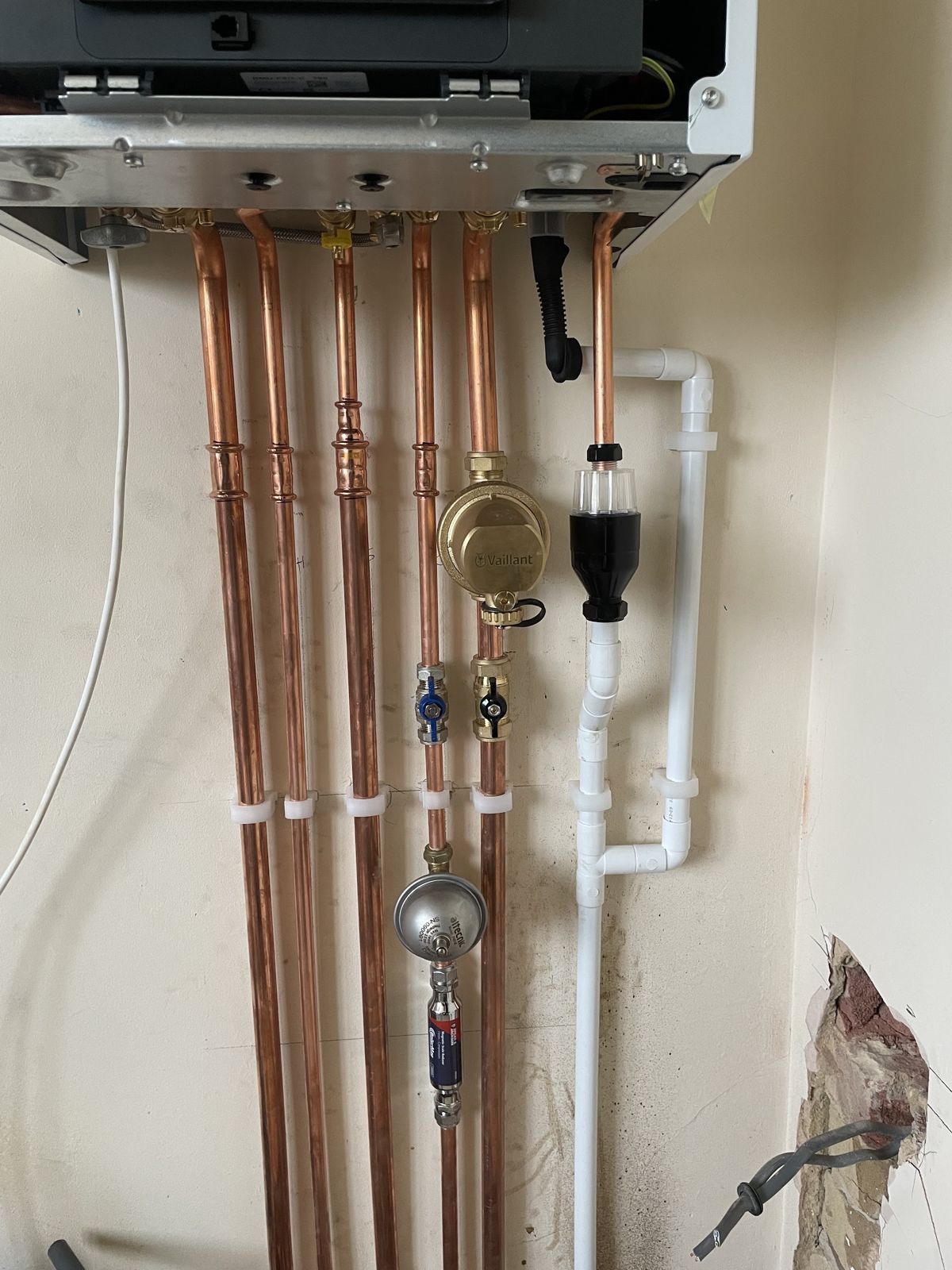 Copper pipework, valves and a filter under a boiler, with the wall still to be finished